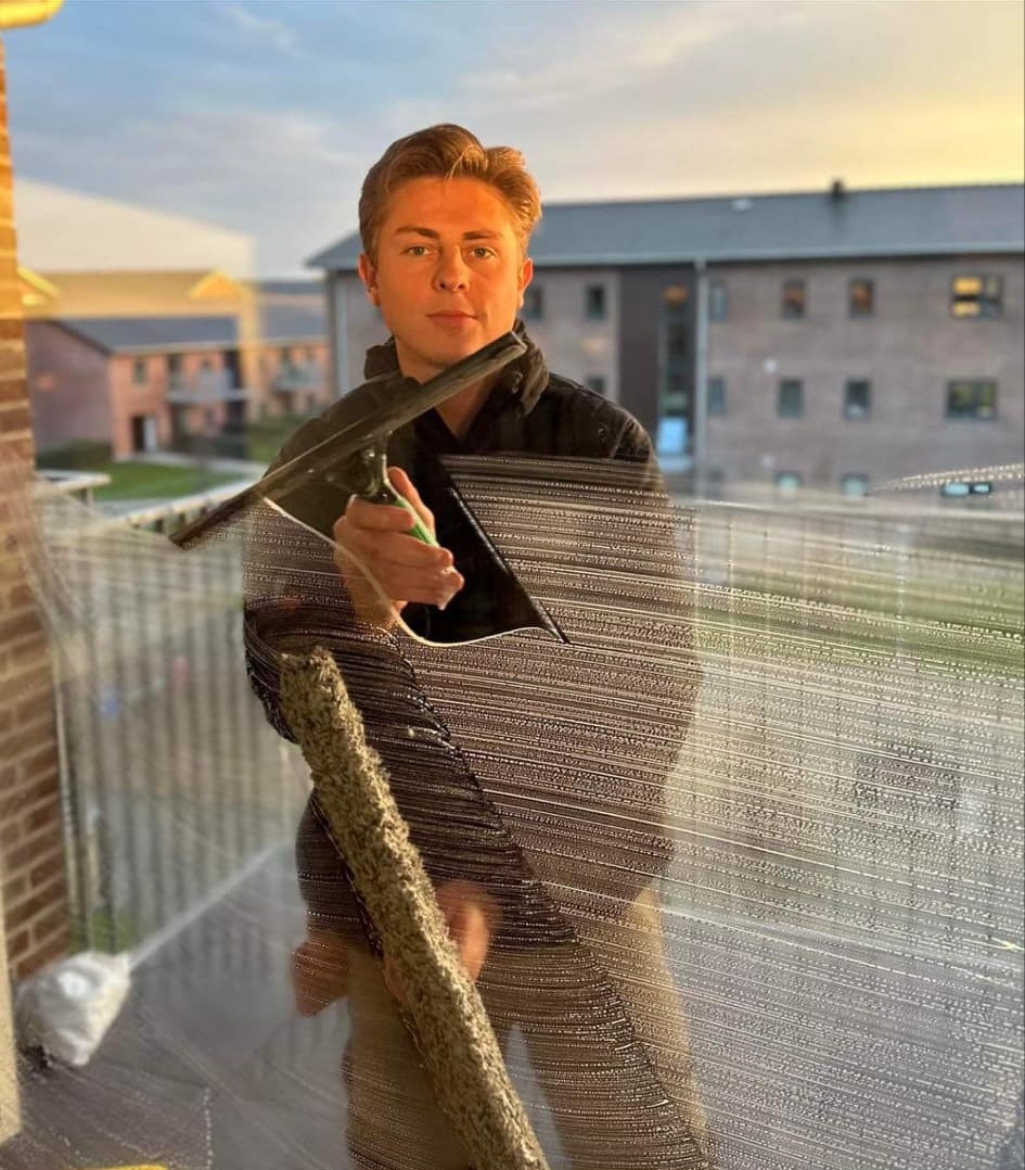 Oscar rengør vinduer med en vinduesskraber og ser mod kameraet – Vinduespudsning Esbjerg