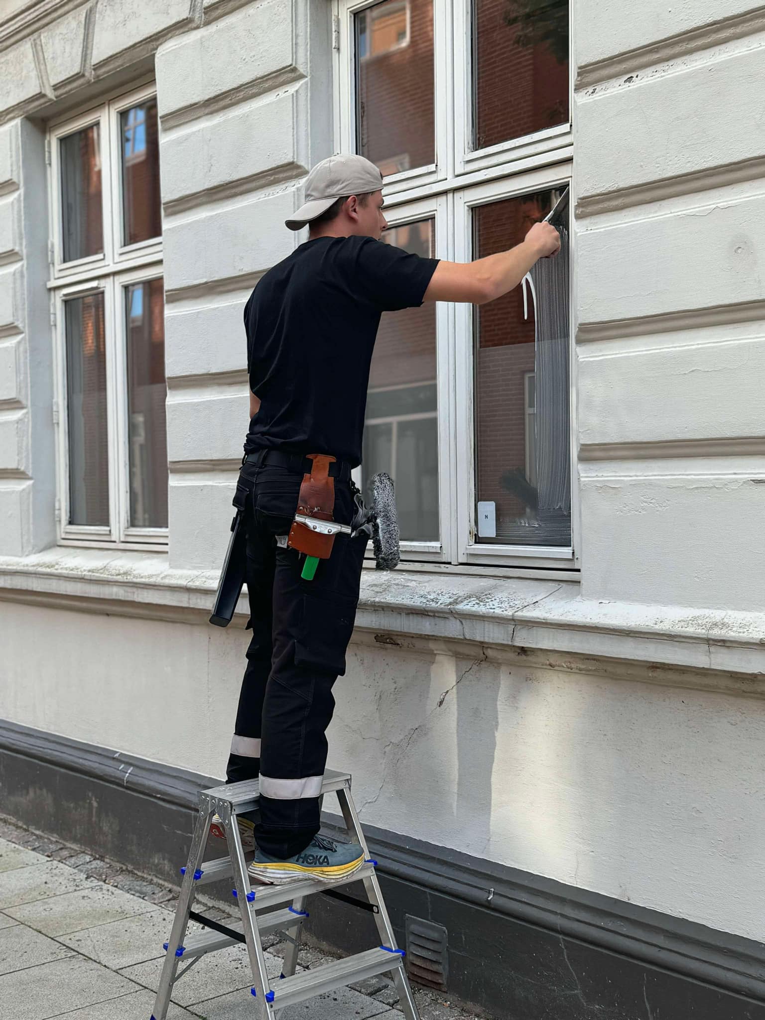 Oscar står på en trappestige og rengør vinduer på et hus – Vinduespudsning Esbjerg